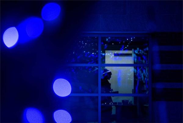  A silhouette of a person in an office is seen from the outside near blue lights. 